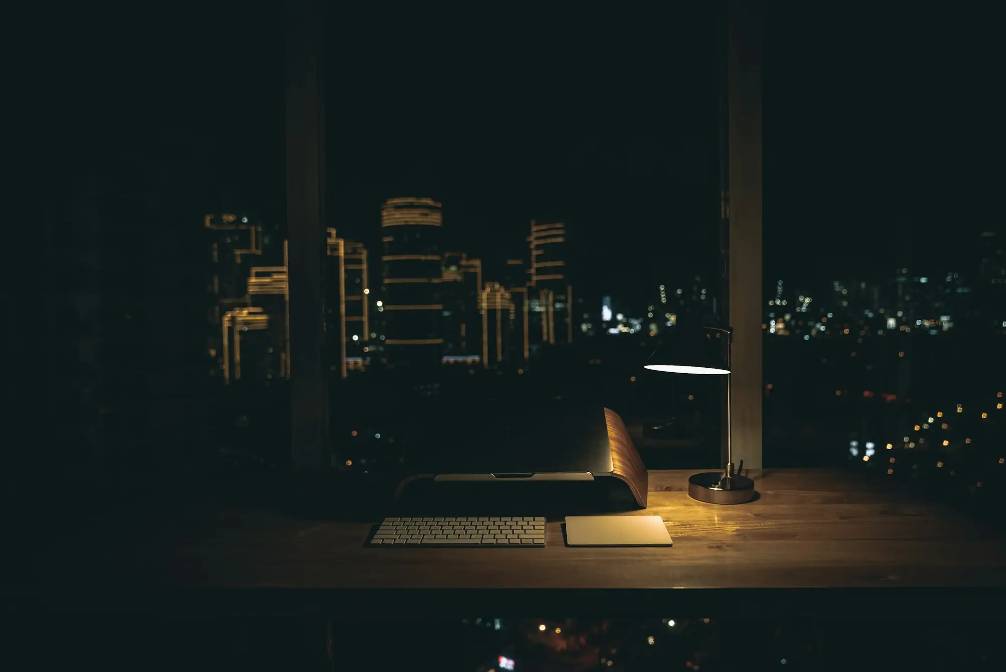 Escritorio con una computadora frente a una ventana con la ciudad de noche