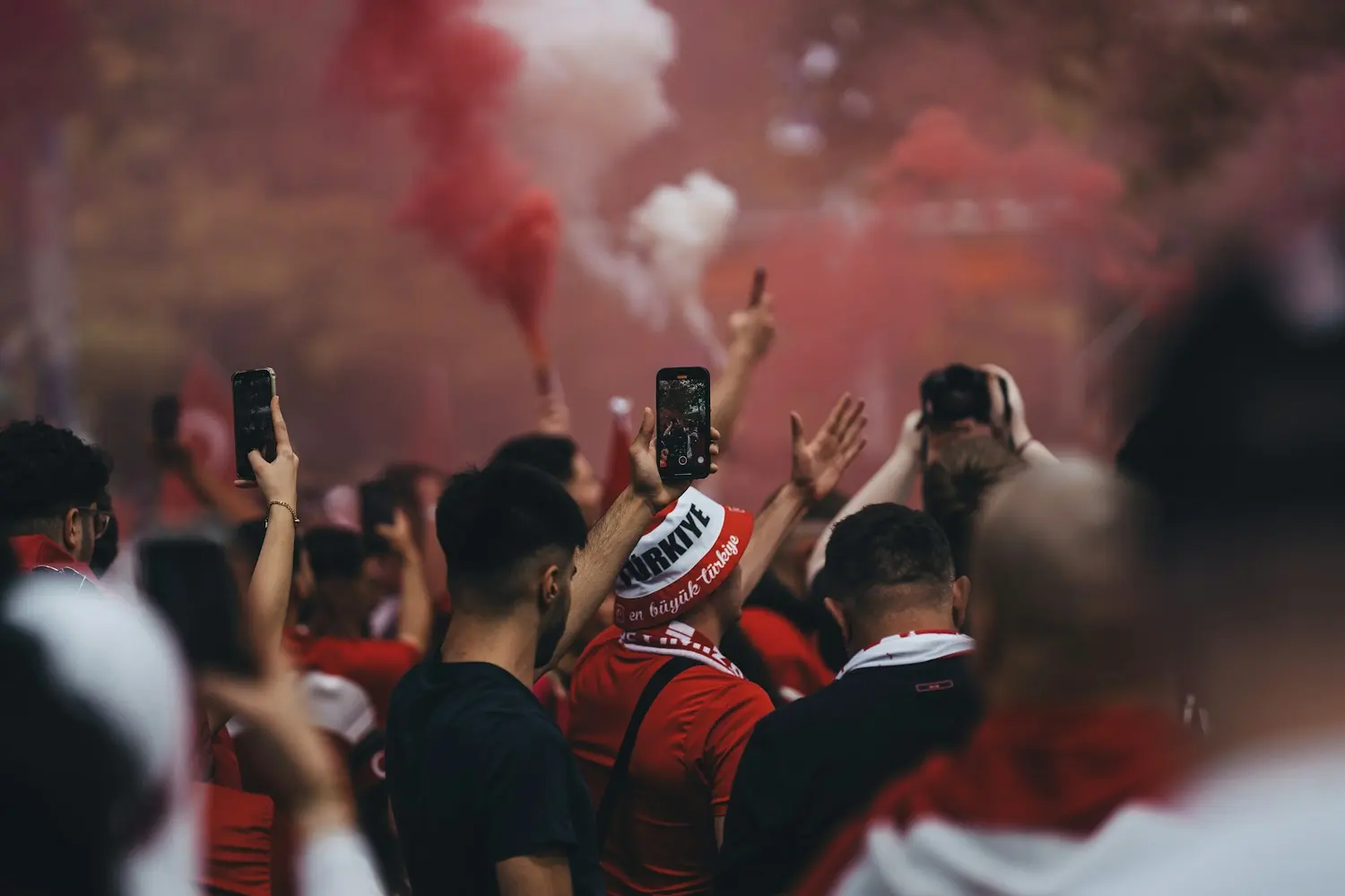 Aficionados entre humo rojo levantando sus teléfonos en la tribuna